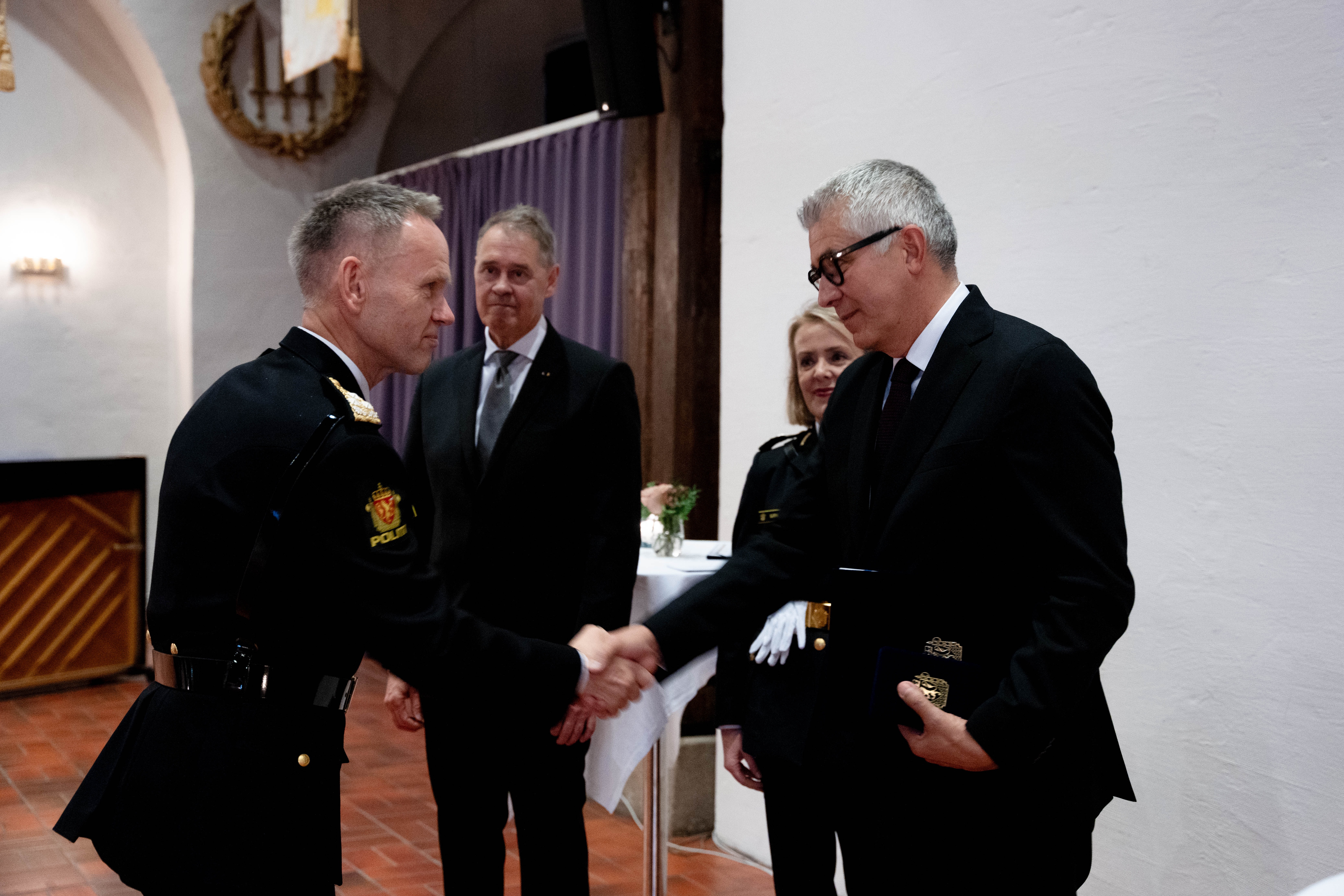 Mann i uniform gir en håndtrykk til mann i dress under utdeling av medalje.