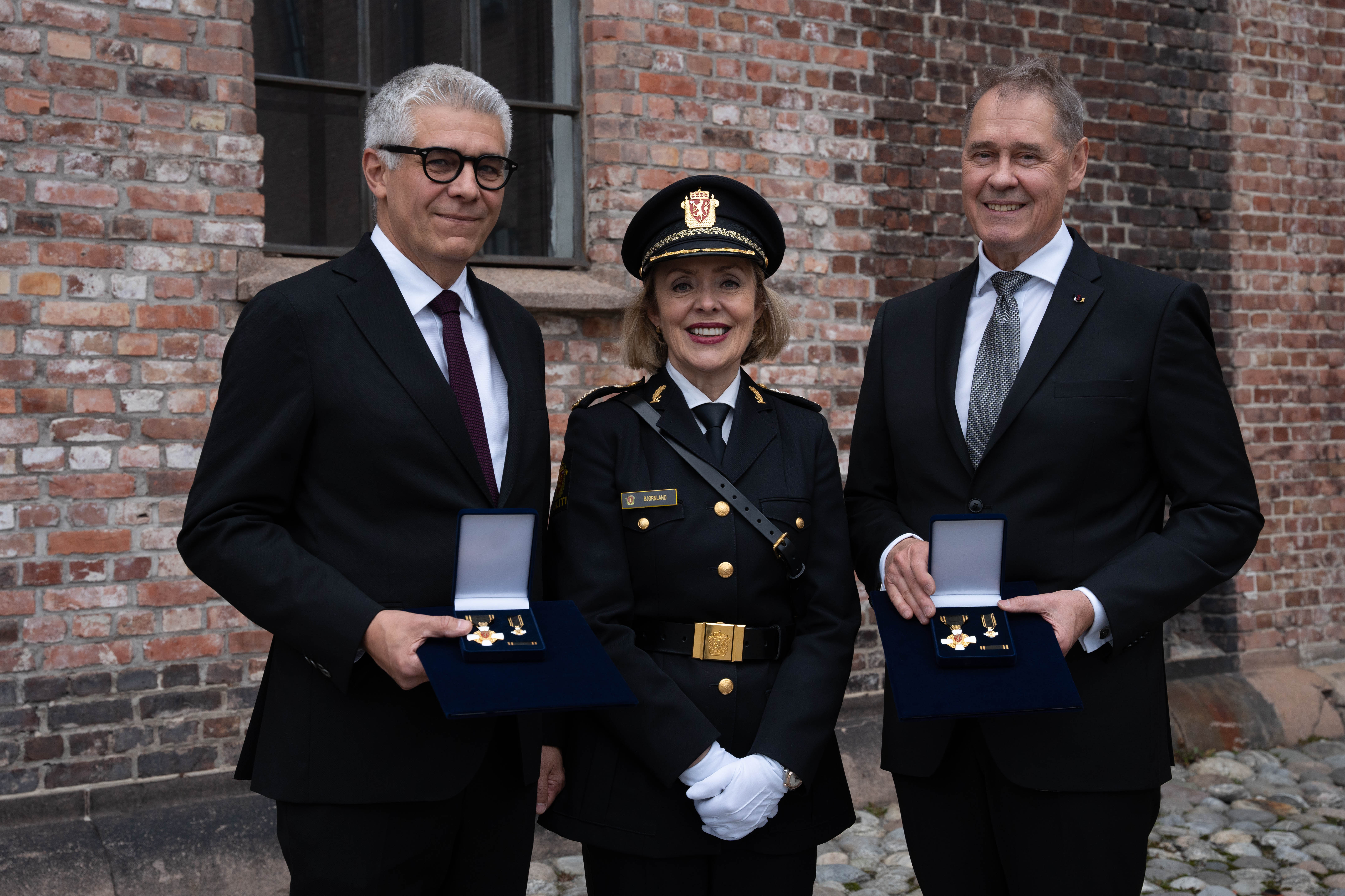 To menn i dress med medalje i hånda, sammen med dame i norsk politiuniform. 